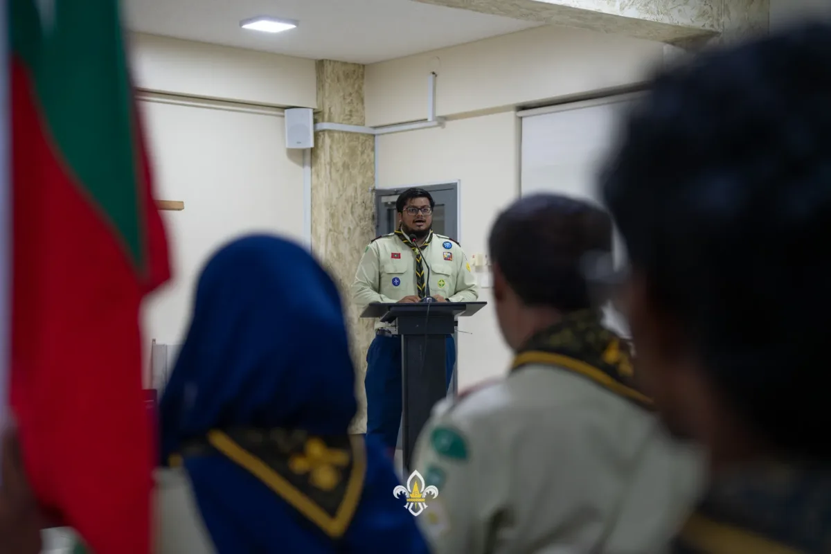The Crew Chairperson delivers the welcome address beside the Scout flags.
