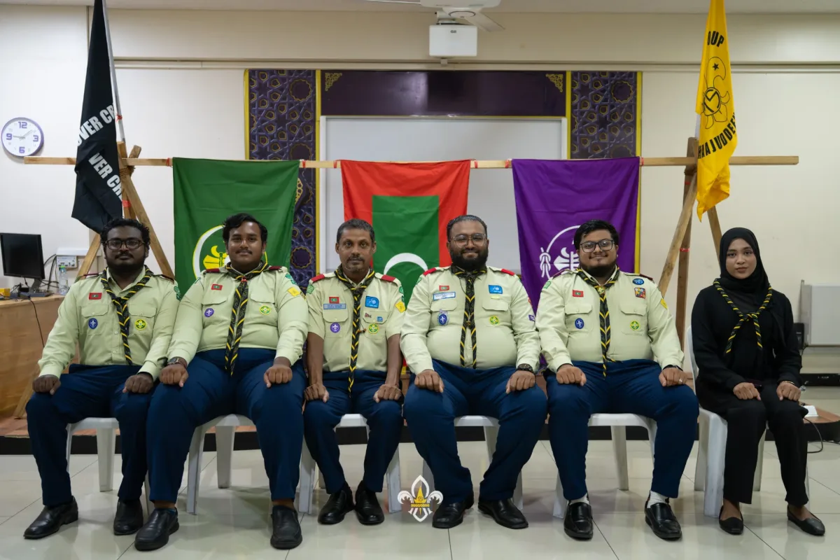 Rovers and leaders sit for a group photograph in front of the Maldives and Scout flags.
