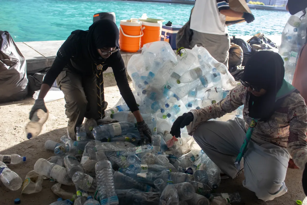Two volunteers sorting plastic bottles into recyclable waste piles near the Hulhumalé Phase 2 waterfront.