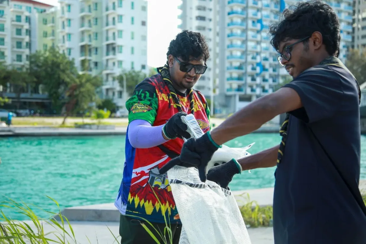 Two Rovers working together to place collected litter into a large white sack beside the Hulhumalé waterfront.